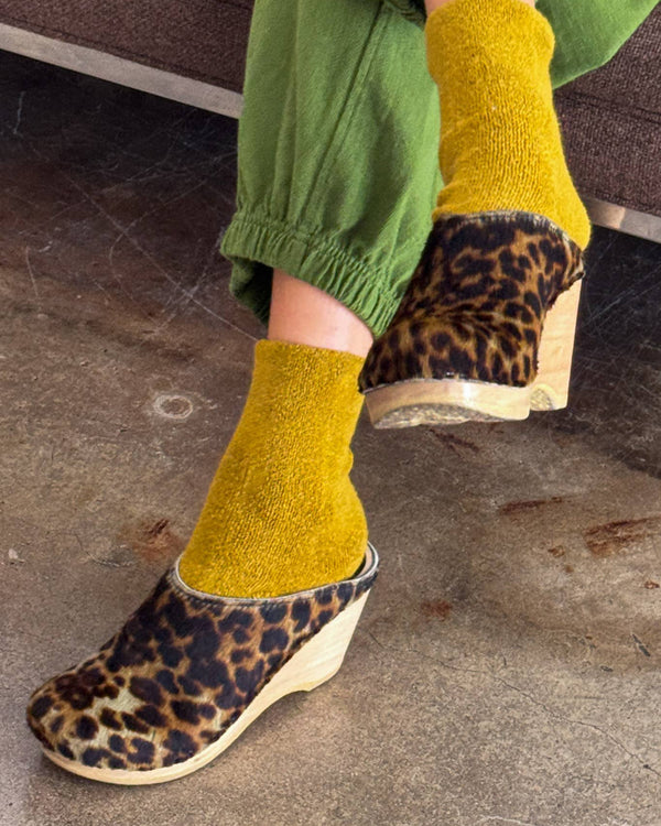 Person wearing mustard yellow socks and leopard print shoes on a concrete floor.