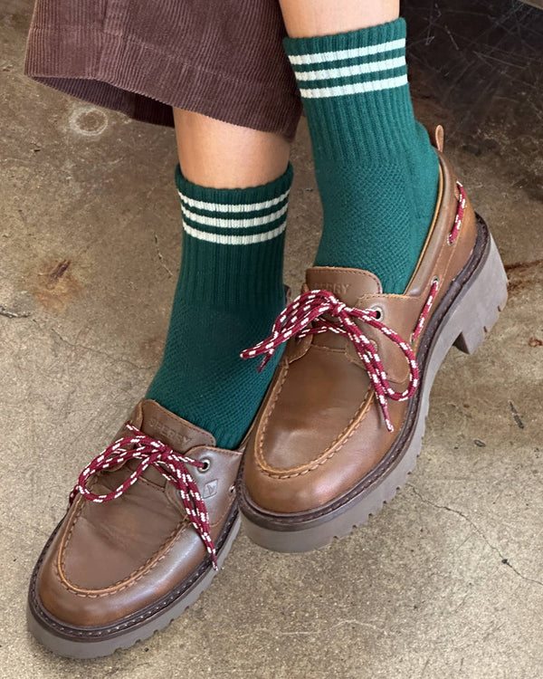 Brown loafers with red laces worn with green socks on a concrete floor.