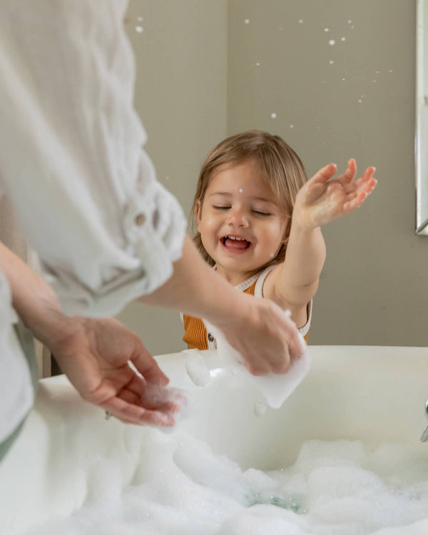 Child playing with bubbles in a sink with an adult nearby