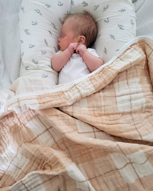 Newborn baby sleeping under a patterned blanket and quilt