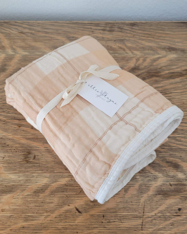 Folded peach and beige plaid blanket with a white label on a wooden surface