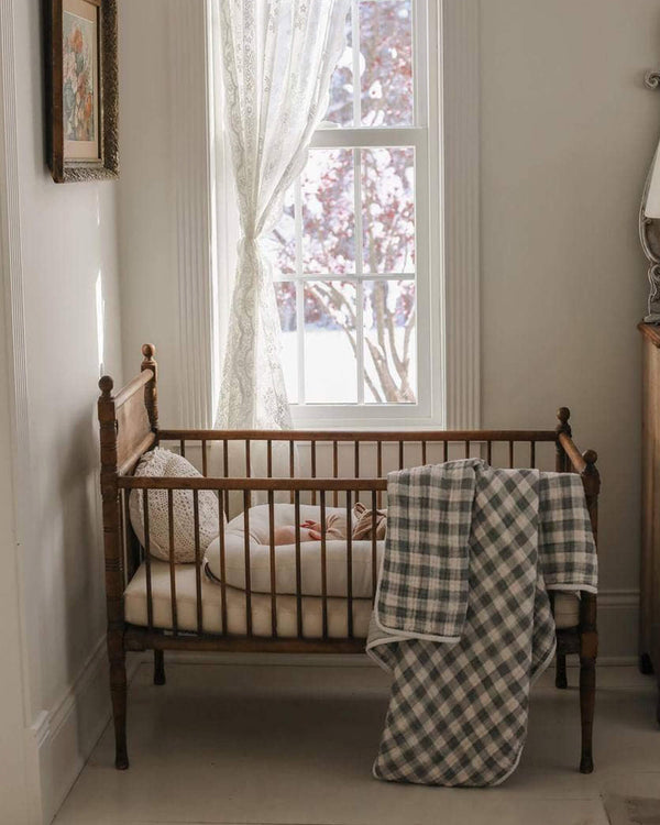 Wooden crib with green gingham blanket in a softly lit room