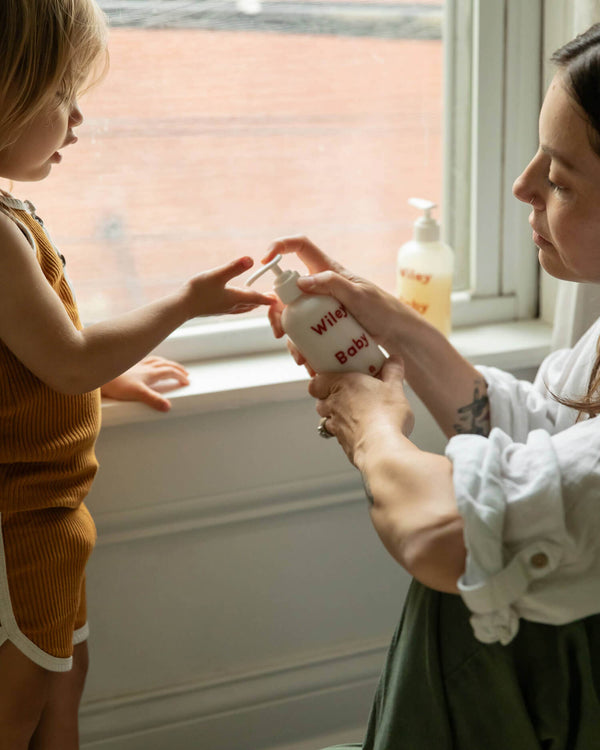 Woman and child holding bottles of 'Wiley Baby' baby lotion by a window.