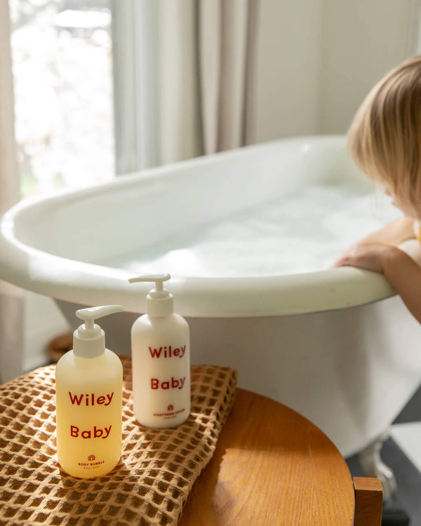 Two bottles of Wiley Baby products on a wooden stool next to a bathtub.