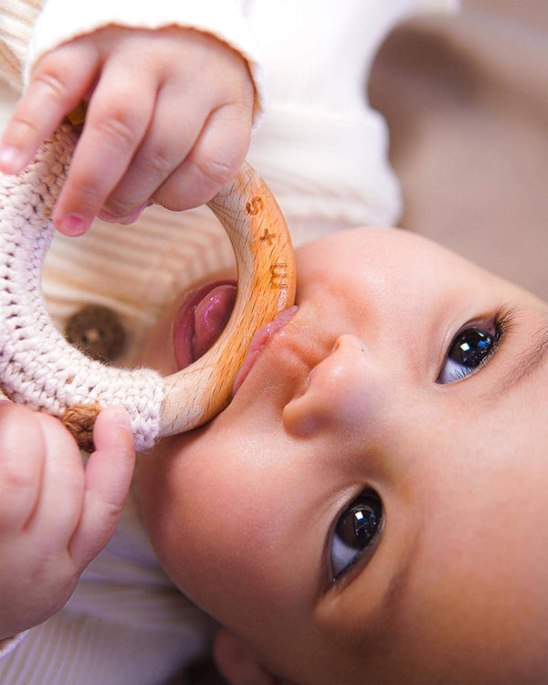 Baby laying down and chewing the wooden ring of a rattle