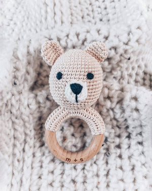 Crocheted bear rattle with wooden ring on a textured beige background
