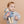 Child wearing a light blue knit sweater holding a teddy bear with goggles and 'SKI' text on a beige background