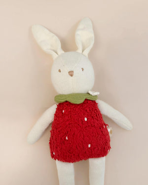 Stuffed bunny toy wearing a red dress with white polka dots on a beige background