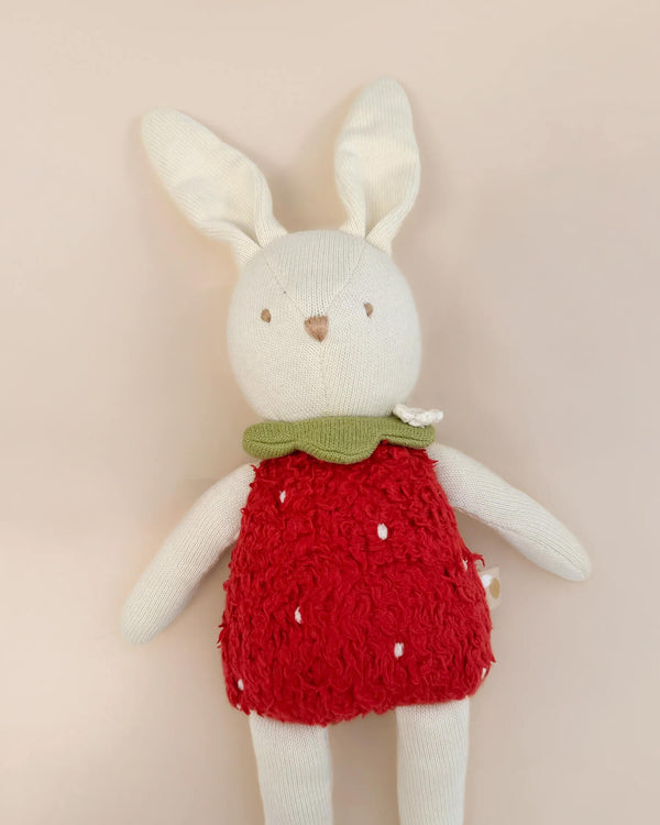Stuffed bunny toy wearing a red dress with white polka dots on a beige background
