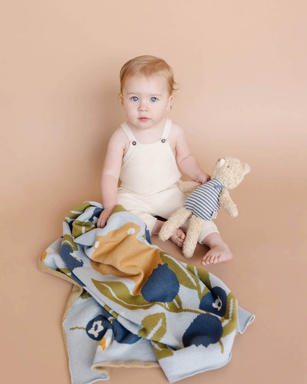 Baby holding a teddy bear with a colorful blanket on a beige background