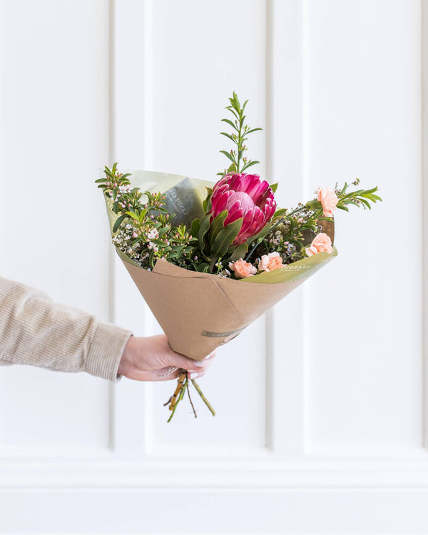 Hand-held Darling Bouquet with a protea focal flower and peach accents, arranged in Landfall’s airy, delicate style in a petite bundle.