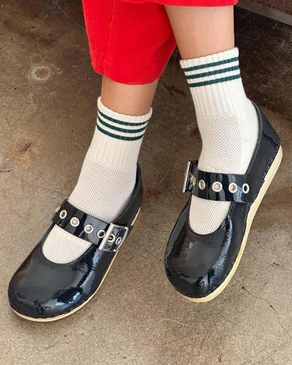 Person wearing navy shoes with buckles and white socks with green stripes on a concrete floor.