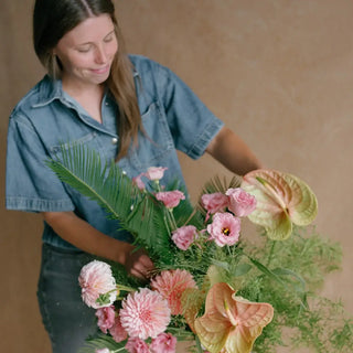 Emily Guin, founder and floral designer of Landfall Floral Co., arranging pink dahlias, anthuriums, and seasonal greenery.