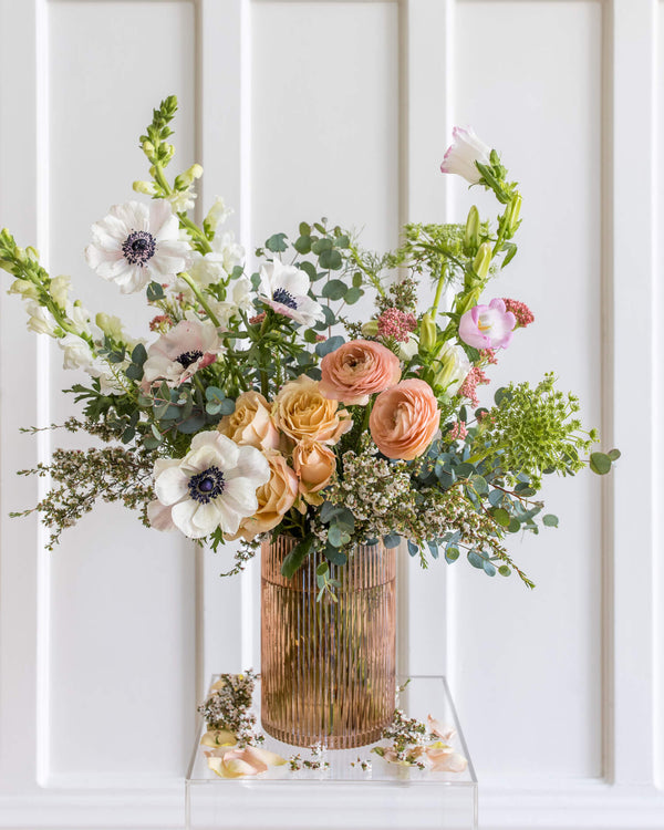 Luxe Arrangement in a ribbed blush glass vase featuring anemones, garden roses, ranunculus, snapdragons, and textural greenery in Landfall’s airy, natural style.