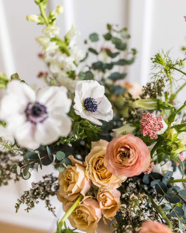 Close-up of the Luxe Arrangement showcasing premium blooms—anemones, roses, and ranunculus—with soft, delicate texture in a blush ribbed vase.