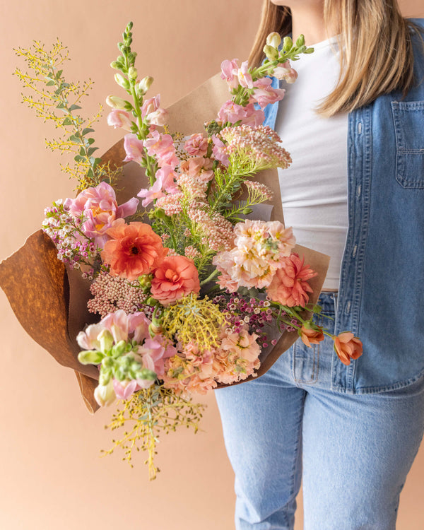 Grand wrapped bouquet for Mother's Day in peach, coral, and soft pink, held for scale — Landfall Floral Co. in Edgewater, Denver.