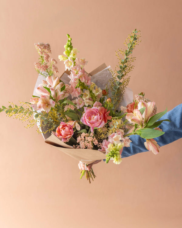Signature wrapped bouquet for Mother's Day in peach and coral with tulips and wild greenery, hand-arranged by Landfall Floral Co.