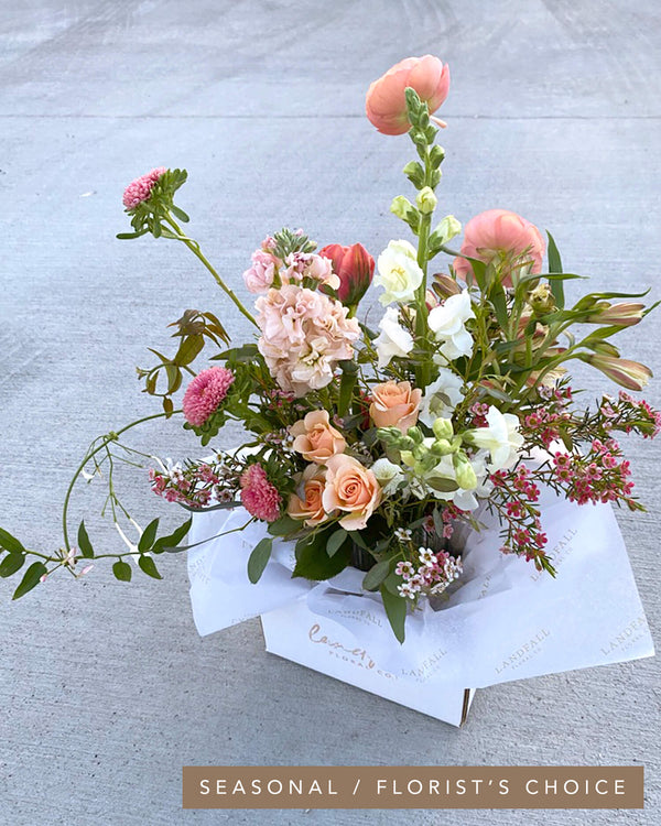 Signature Arrangement in a seasonal palette featuring spray roses, aster, stock, snapdragons, jasmine vine, and ranunculus in soft peach tones, designed in Landfall’s airy, delicate style.