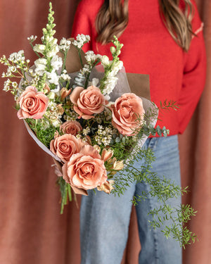 Lovestruck Valentine’s Day Bouquet in the rose-forward style, held by a person in jeans and a red sweater, arranged in a romantic palette of blush, ivory, caramel, and soft reds.