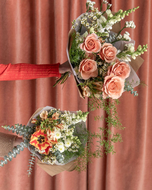 Side-by-side comparison of the Lovestruck rose bouquet and The Luckiest Signature Bouquet, showing the fuller, grander scale of Lovestruck against a rosy backdrop.